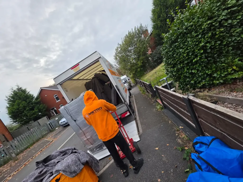 A Metro Man and van team member expertly loading a fully shrink-wrapped item onto a tail lift, showing how to handle a Manchester winter move in grim weather.